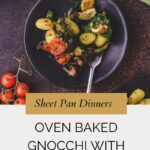A black plate with oven-baked gnocchi, roasted tomatoes, broccoli, and pesto sits on a brown table. Fresh basil and cherry tomatoes are nearby. Text below reads Oven Baked Gnocchi with Pesto.