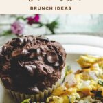 A close-up of gluten-free chocolate chip muffins with chocolate chips next to scrambled eggs with vegetables on a plate. Text above reads “Soft & Fudgy Chocolate Hazelnut Muffins Brunch Ideas.”.