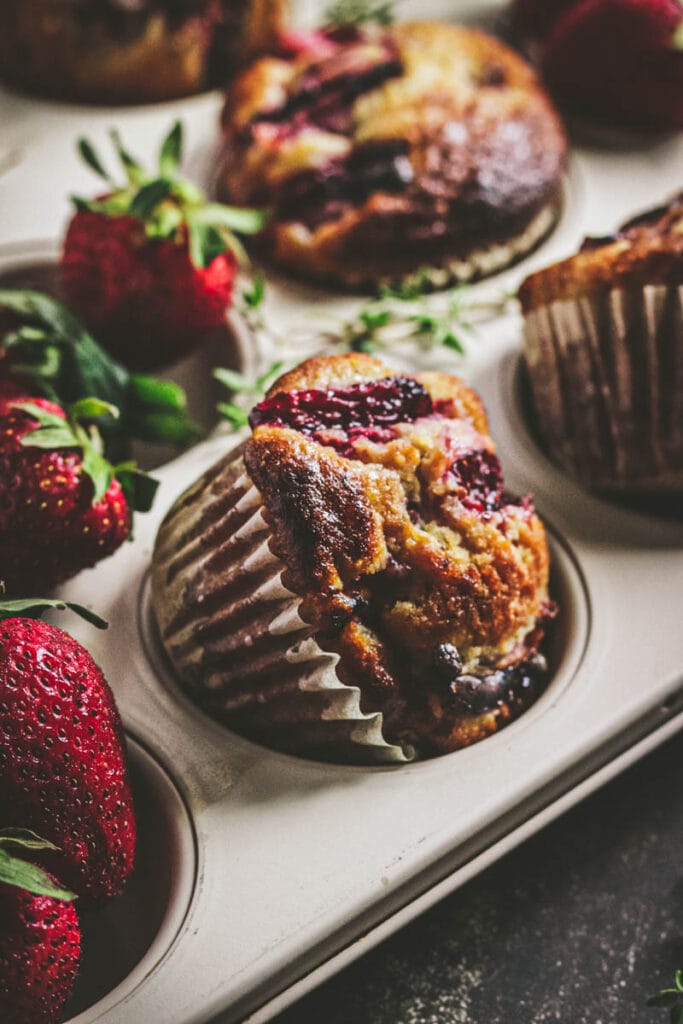 close up of muffin in the pan with strawberries around it