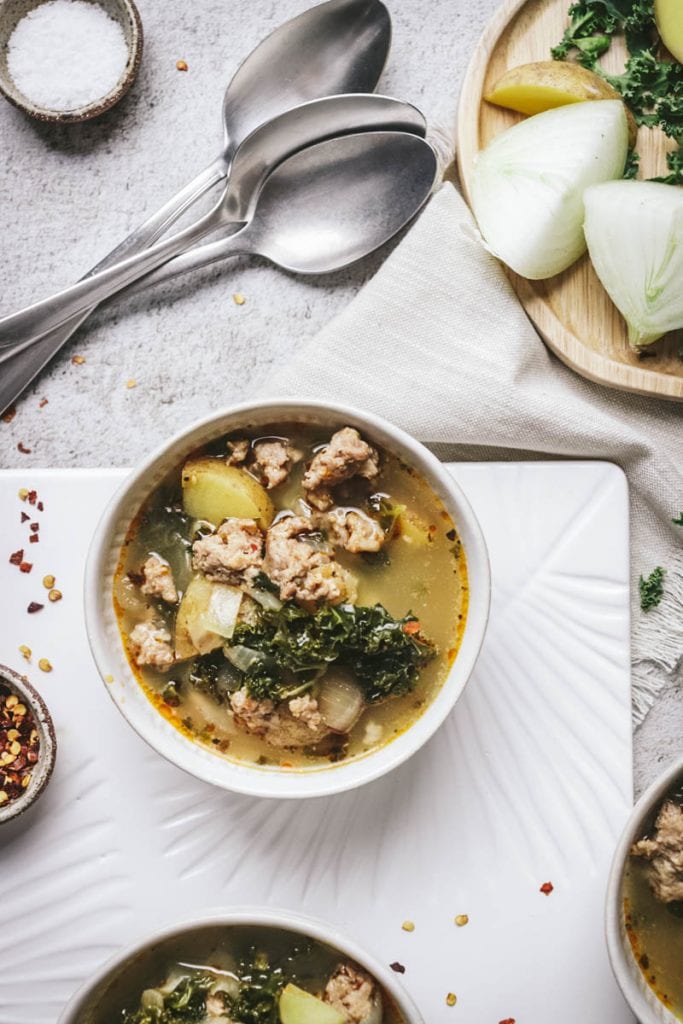bowls of soup in a white bowl with onion and kale and spoons