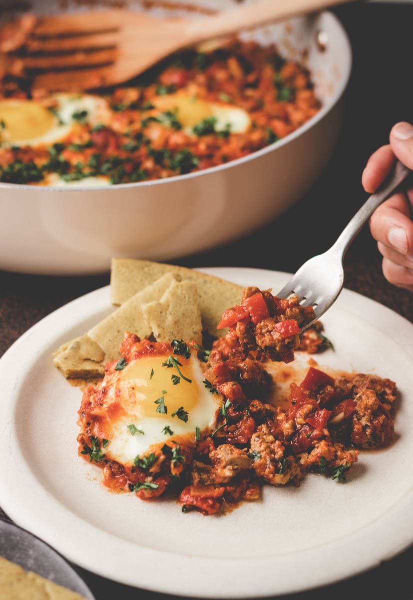 close up shakshuka with ground turkey on a fork over a plate .