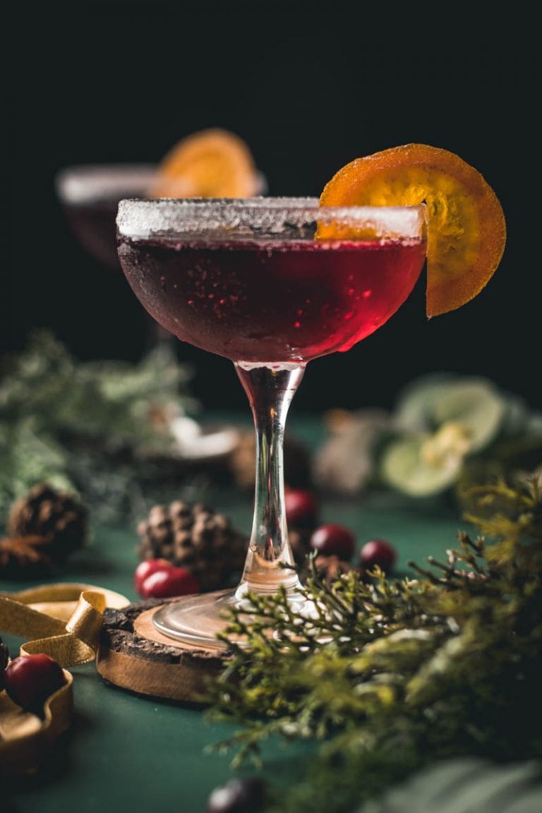 cranberry mocktail on a wood coaster with cranberries, pine needles, pine cones and an orange garnish