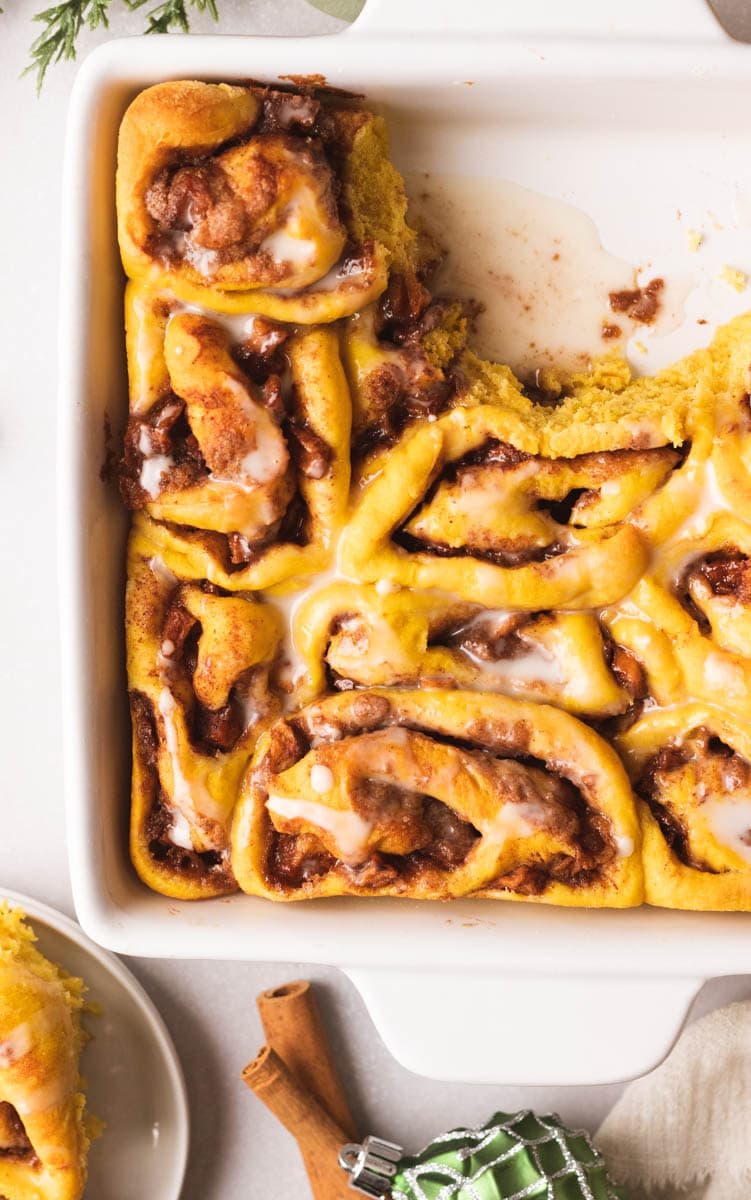 cinnamon rolls in a white baking dish, partially eaten