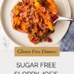 A halved baked sweet potato topped with sugar free sloppy joe’s meat filling sits on a white plate. A spoon scoops the hearty mixture. Text below reads: Gluten Free Dinners: Sugar Free Sloppy Joe’s.
