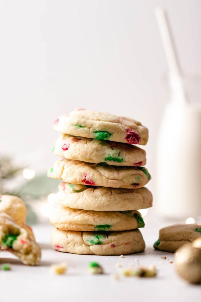 Stack of Christmas M&M cookies with crumbs and milk in the background.