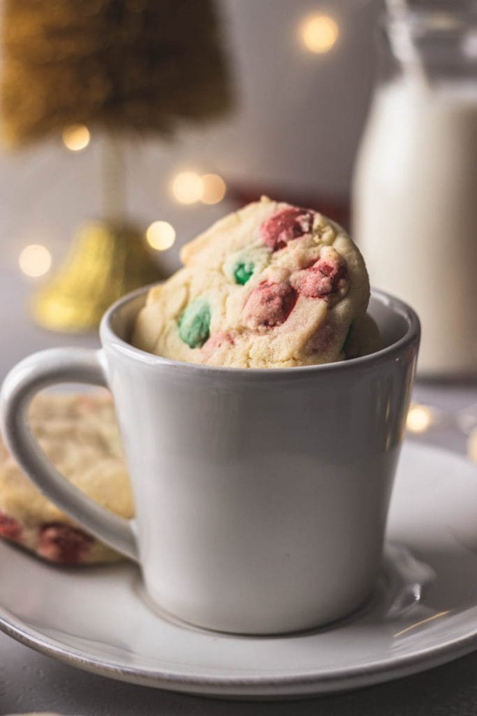 Cookies in a mug on top of a saucer with milk in the background .