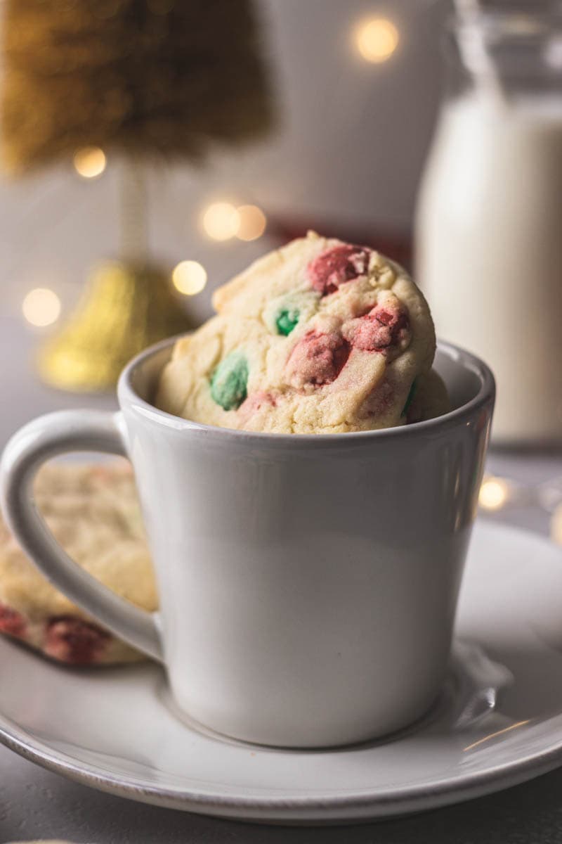 Cookies in a mug on top of a saucer with milk in the background .