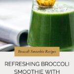 A green broccoli smoothie with mango in a glass, garnished with a yellow flower, sits on a table beside an open book. Text reads: Refreshing Broccoli Smoothie with Mango.