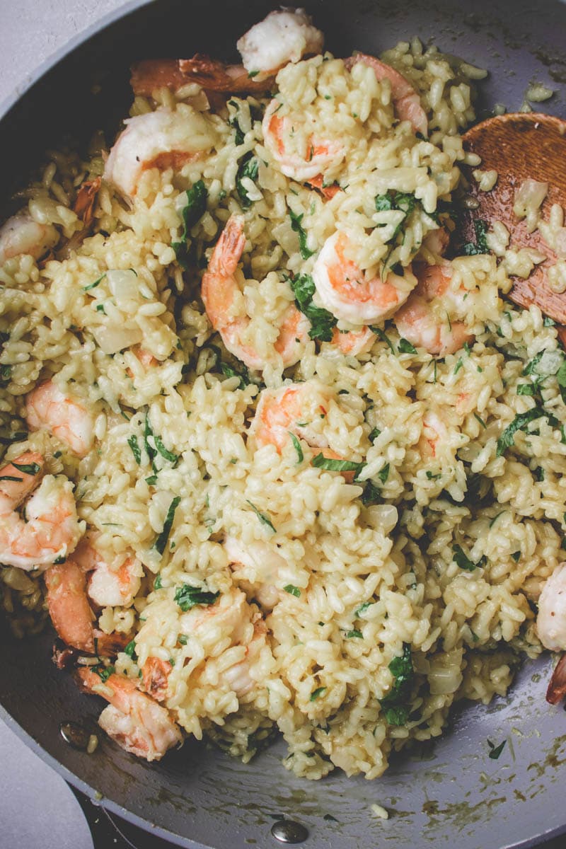 A skillet filled with creamy shrimp and zucchini risotto, mixed with chopped spinach and onions. A wooden spoon rests in the pan, suggesting the dish is freshly cooked and ready to serve.