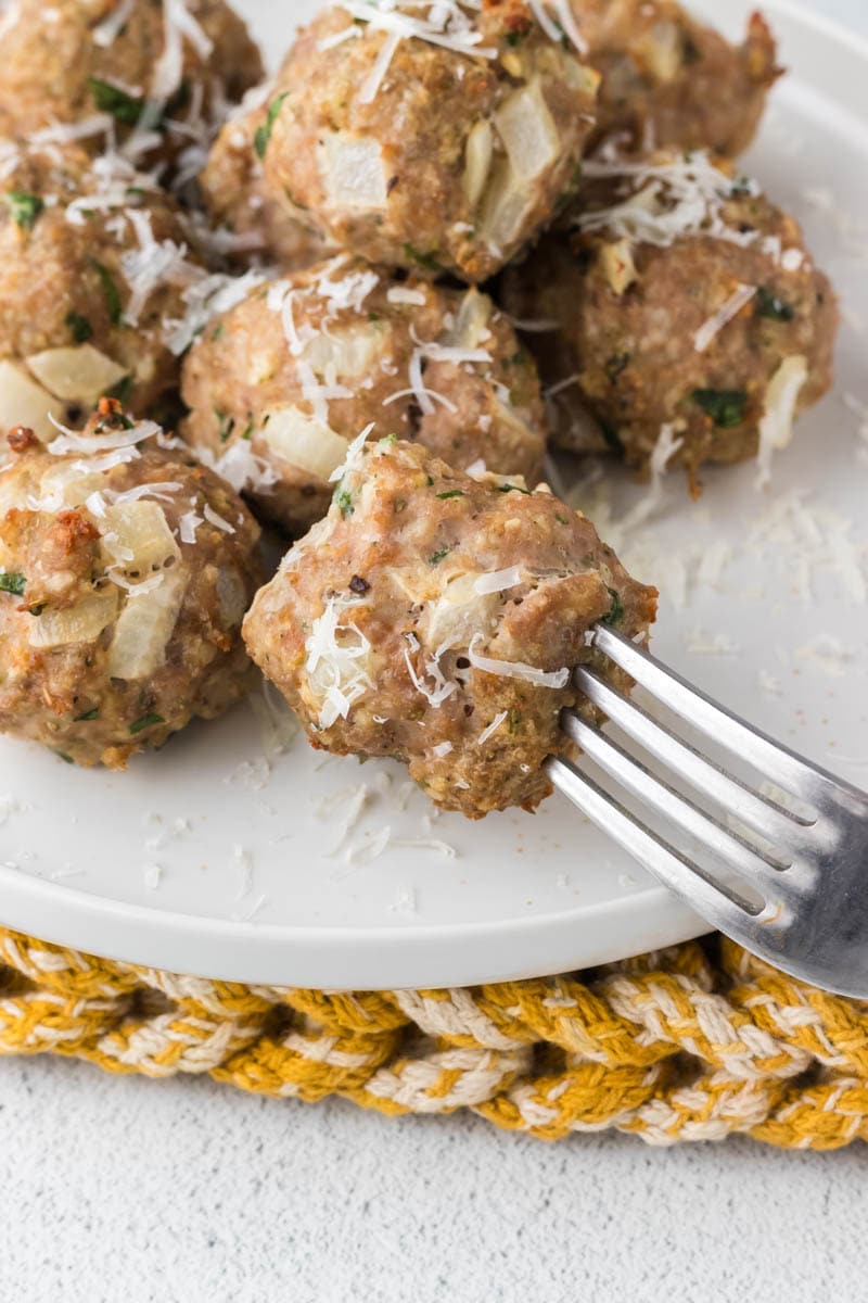 Meatball on a fork with a plate of meatballs.