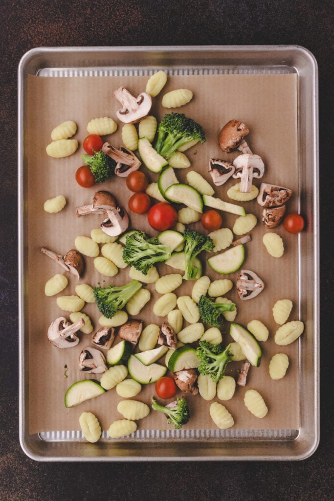 Process shot of gnocchi with pesto and vegetables. Gnocchi and veggies on a sheet pan.