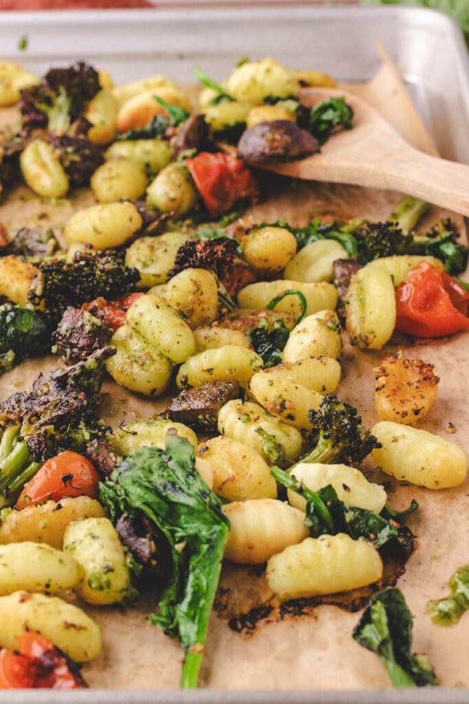 Gnocchi and veggies on a sheet pan with a serving spoon.
