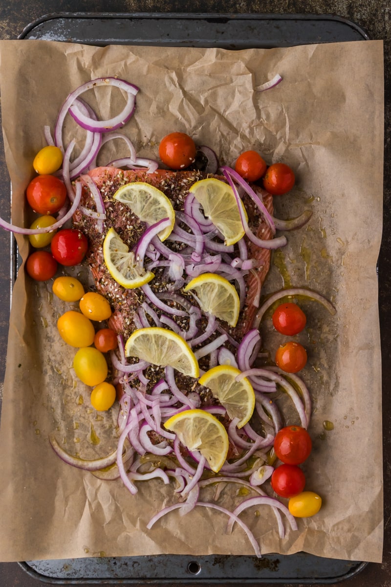 salmon on a sheet pan with spices, red onion, lemon slices and baby tomatoes.