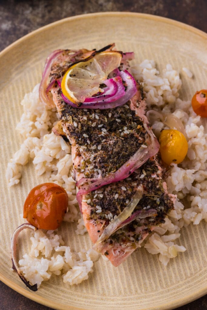 middle eastern salmon on top of brown rice on a yellow plate.
