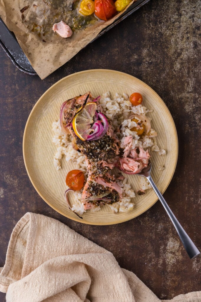 middle eastern salmon on top of brown rice on a yellow plate with a fork and linen.