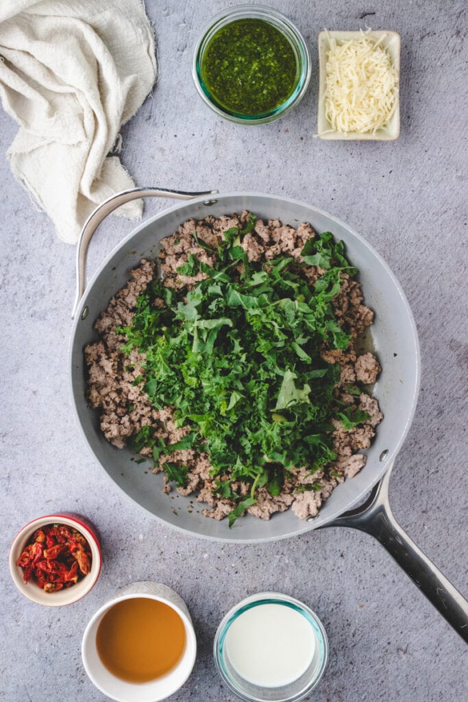 Adding kale to the cooked ground turkey in a large skillet.
