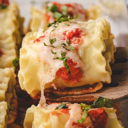A close-up of a cheesy turkey lasagna roll up topped with tomato sauce and chopped fresh basil, being lifted from a glass baking dish with a wooden spatula.