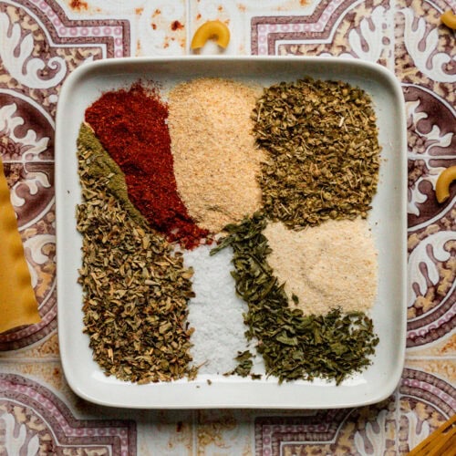 zesty italian seasoning on a white plate with pasta noodles around it.