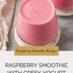 Two glasses filled with raspberry smoothie with Greek yogurt sit on a gray surface, a beige cloth nearby. Text reads Raspberry Smoothie Recipes – Raspberry Smoothie with Greek Yogurt.