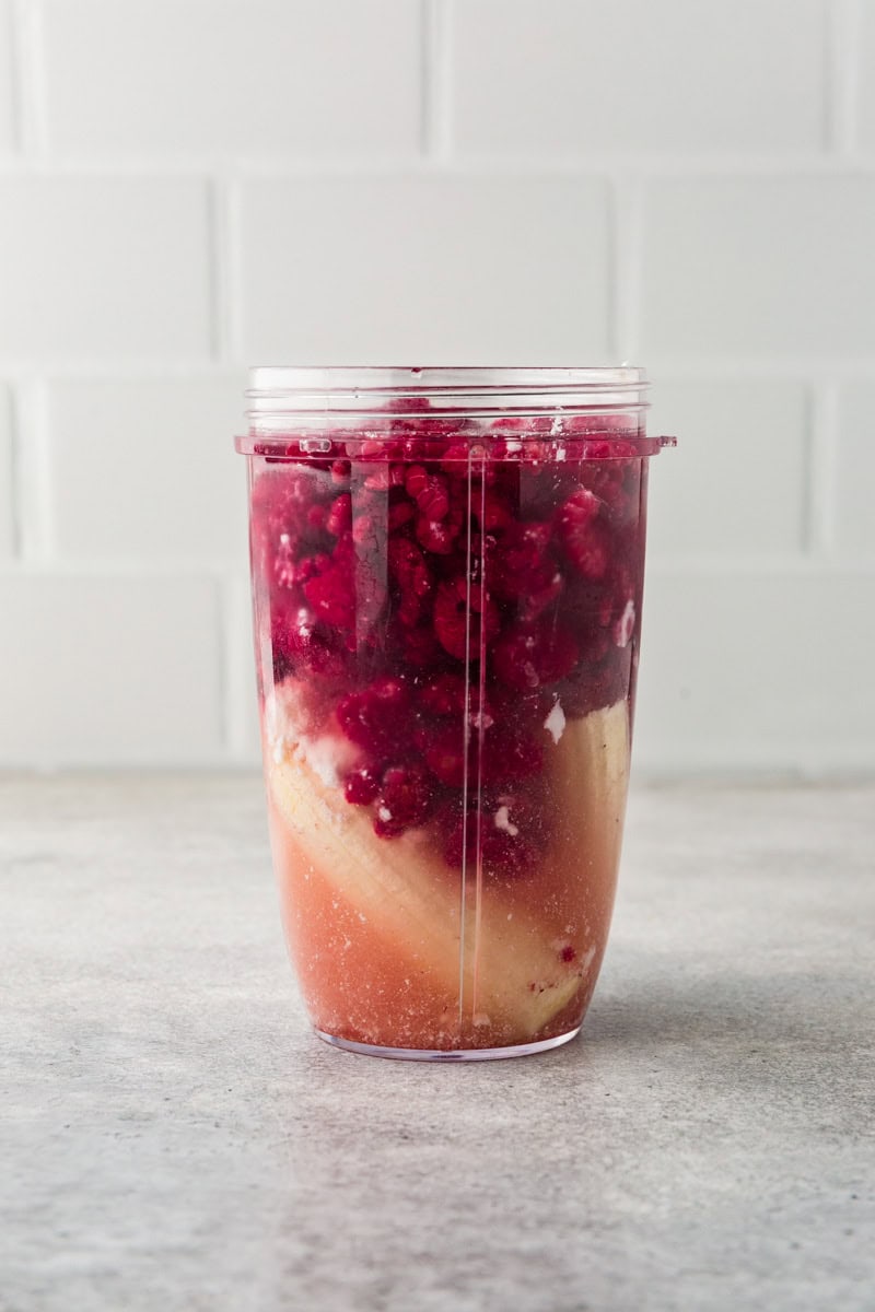 all the ingredients for a raspberry greek yogurt smoothie in a nutri bullet blender.