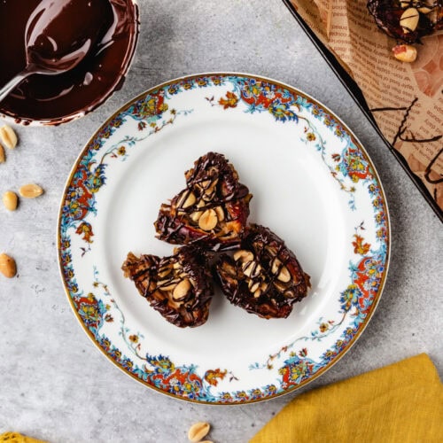 3 dessert dates on a flower rimmed plate with melted chocolate in a bowl.