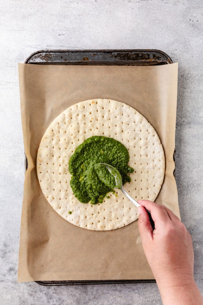 adding pesto to pizza crust.