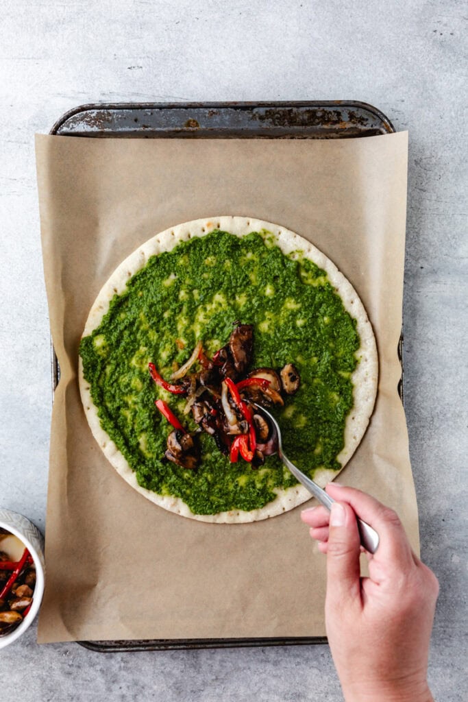 adding veggies to pizza crust.