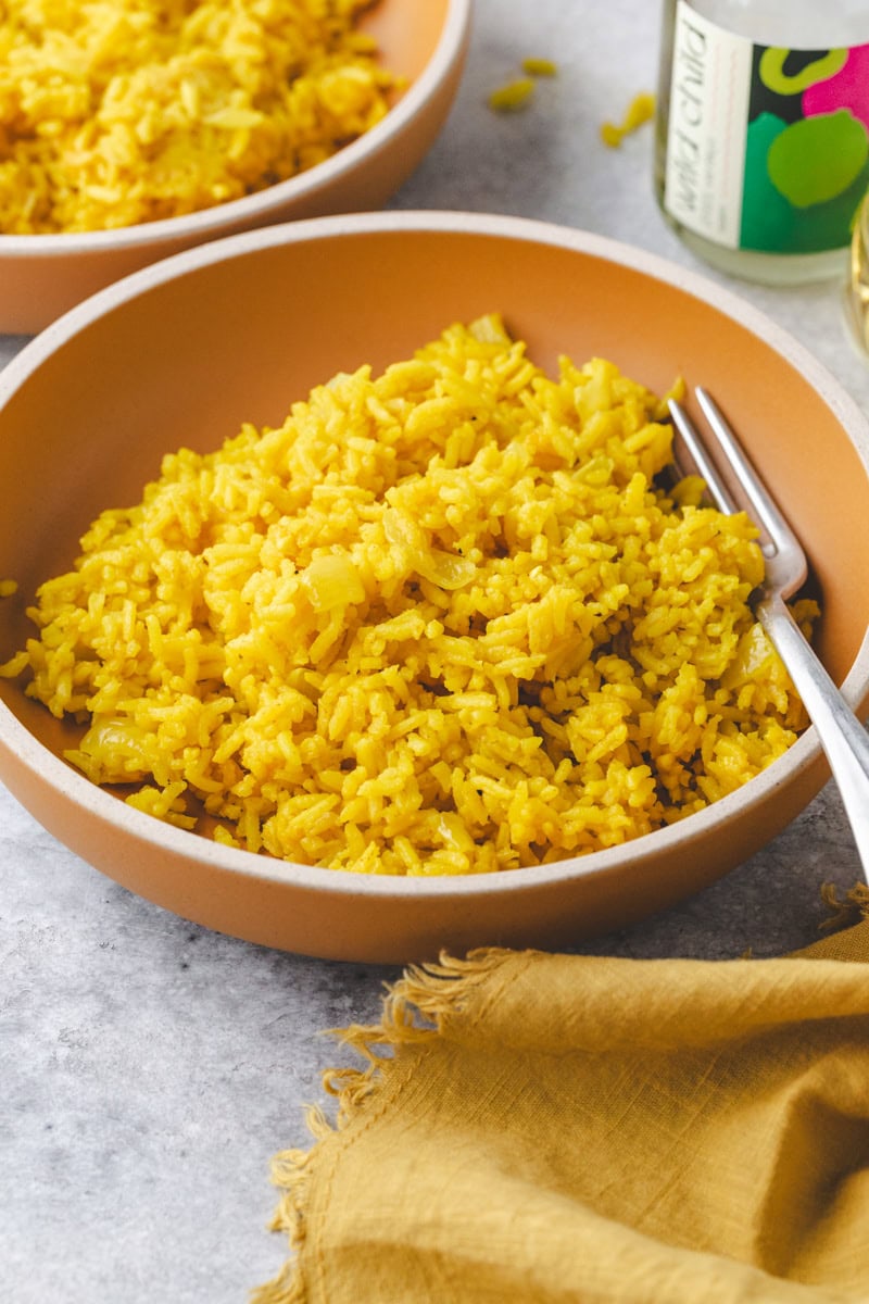 garlic turmeric rice in a bowl with a fork and a glass of wine.