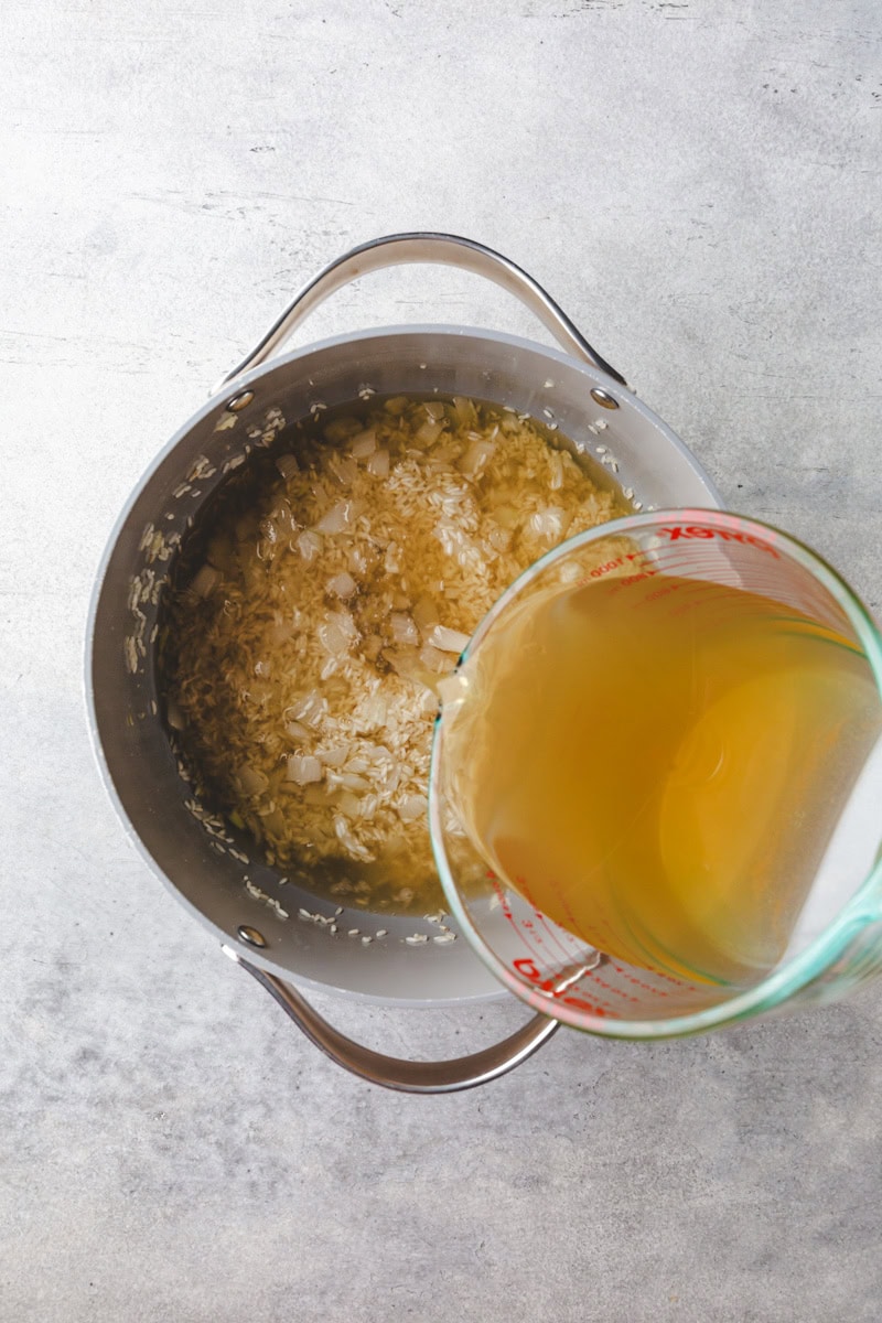 pouring broth into a pot of rice.