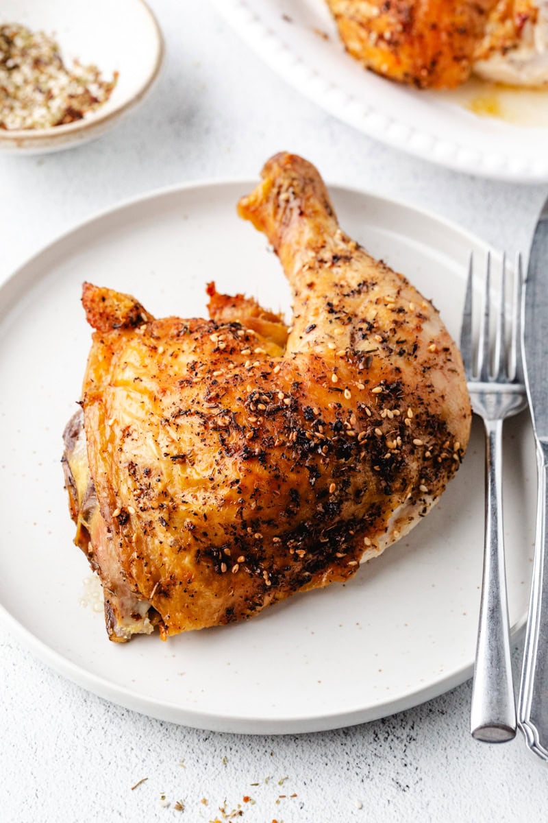piece of roasted chicken on a plate with a knife and fork. 