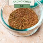 A bowl filled with a dark spice blend labeled Homemade Ancho Rub is displayed on a light textured surface, enticing culinary explorers. The website whensaltyandsweetunite.com is noted at the bottom.