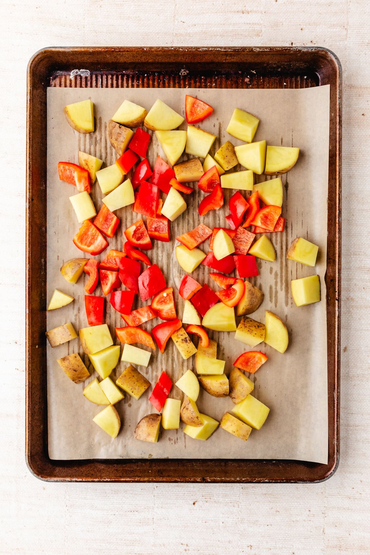 Chopped red bell peppers and potatoes are artfully arranged on a parchment-lined baking sheet, ready for roasting.