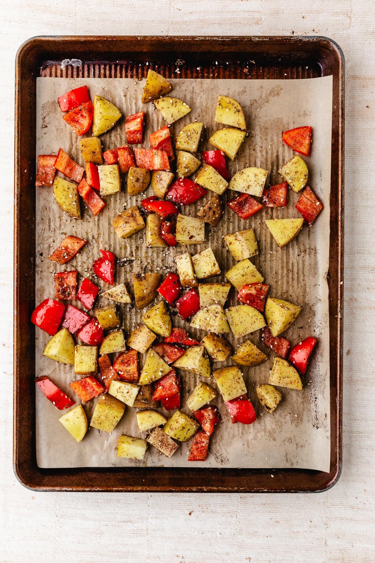 A baking tray with diced red and yellow bell peppers and potatoes seasoned with black pepper, on parchment paper. The vegetables are roasted to perfection, showcasing a vibrant medley of colors on a light-colored background.