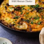 A skillet with a golden Spanish tortilla topped with chopped herbs sits on a counter—perfect for your tapas dinner party. Try this Spanish Tortilla With Mexican Chorizo, one of the best things to do in a power outage. A bowl of herbs and a napkin are beside it.