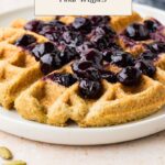 A plate of almond flour waffles with pumpkin seeds, topped with a blueberry compote. Text overlay reads: Healthy Waffle Recipe: Pumpkin Seed & Almond Flour Waffles. Website: whensaltyandsweetunite.com.