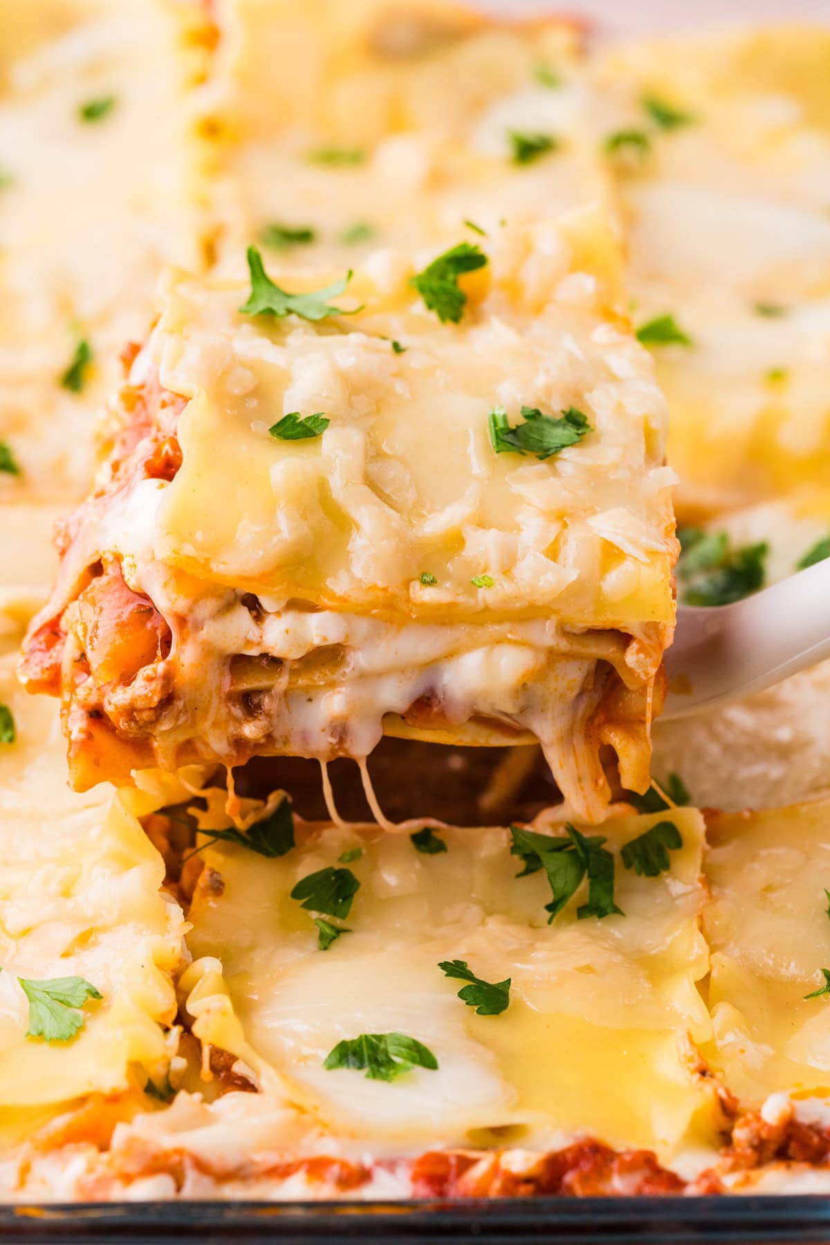 A close-up of a slice of cheesy Ground Turkey Lasagna being lifted from a baking dish, with melted cheese stretching and fresh parsley sprinkled on top.