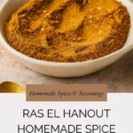 A shallow white bowl filled with a golden-brown Ras El Hanout spice blend sits on a light surface. Text below reads RAS EL HANOUT HOMEMADE SPICE SEASONING and includes a website link.