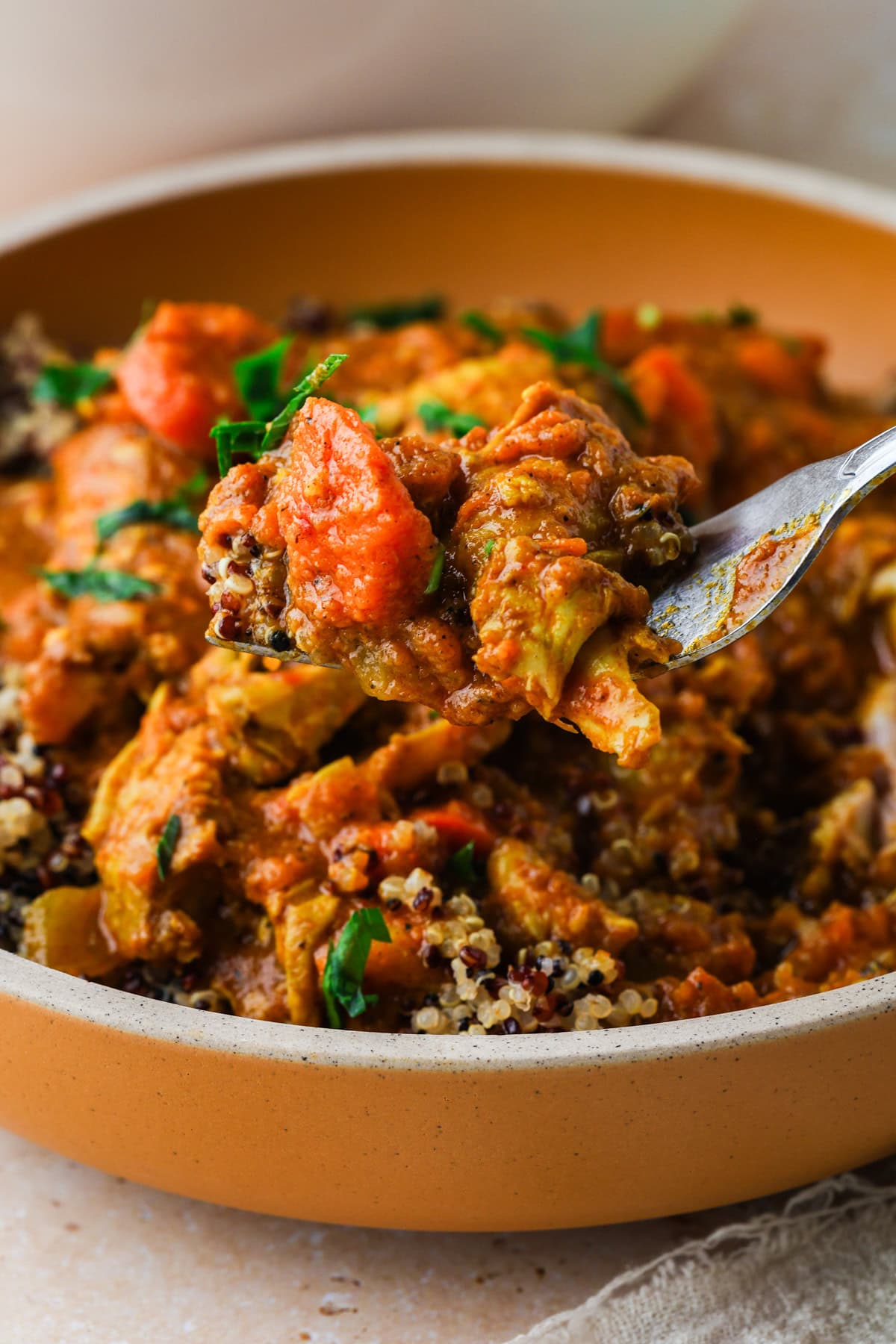 A close-up of a fork holding a bite of vegetable curry with quinoa from a bowl, alongside chunks of vegetables in a creamy, orange-colored sauce, reminiscent of the heartiness found in chicken wing stew and garnished with fresh herbs.
