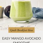 A glass of mango avocado smoothie sits on the countertop beside a halved avocado, a small cup, and a blue cloth. Text reads: Quick Breakfast Ideas - Easy Mango Avocado Smoothie for a nutritious start.