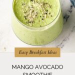 A glass of mango avocado smoothie topped with hemp seeds sits on a light surface. Text reads Easy Breakfast Ideas: Mango Avocado Smoothie and whensaltyandsweetunite.com at the bottom.