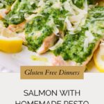 Close-up of pesto salmon fillets baked to perfection, topped with green homemade pesto and grated cheese, garnished with lemon slices. Text overlay reads: Gluten Free Dinners - Salmon with Homemade Pesto.