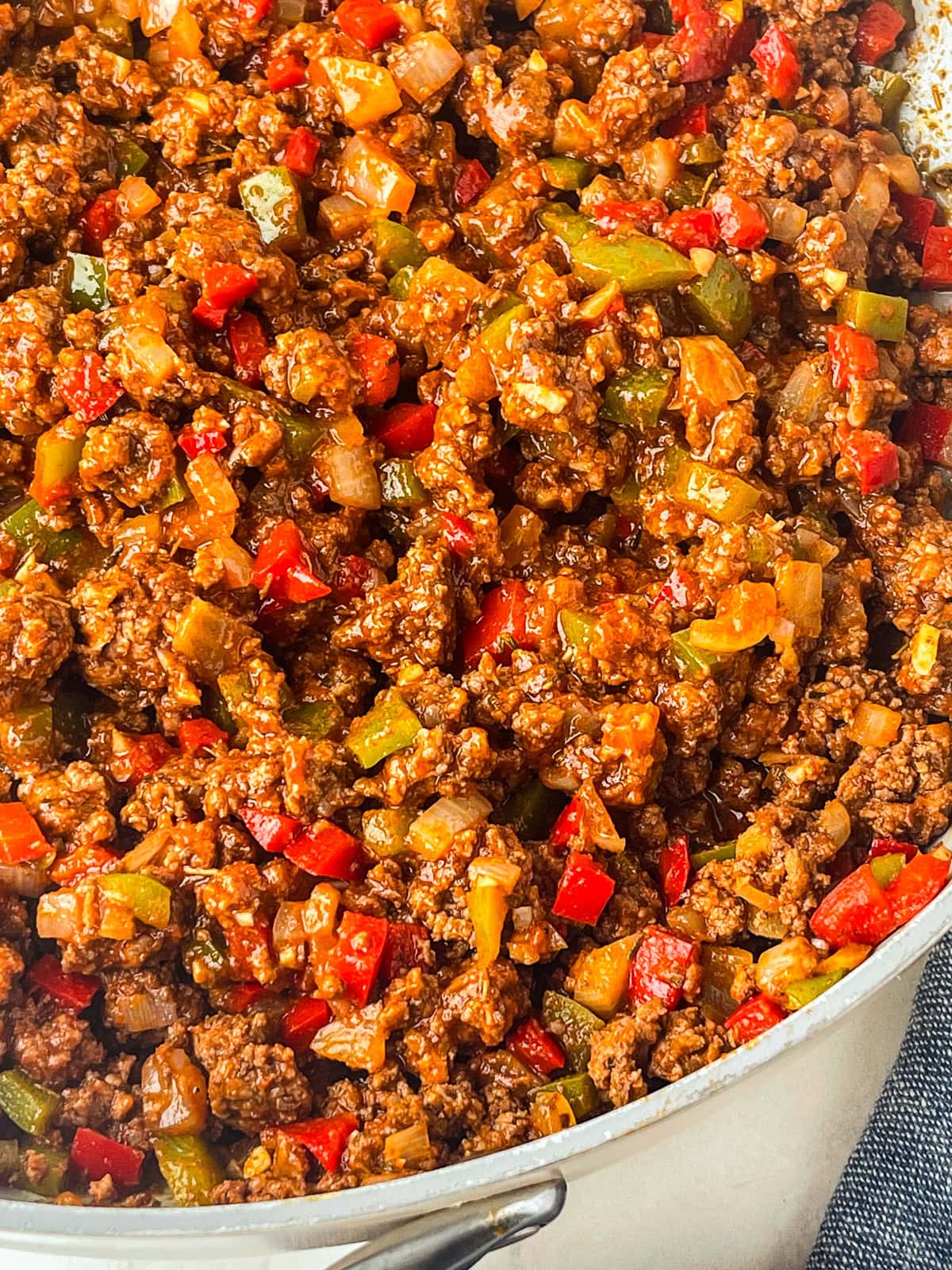 A close-up of a pot filled with cooked ground beef mixed with chopped red and green bell peppers and onions in a rich, savory, sugar free sloppy joe's sauce.