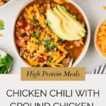 A bowl of ground chicken chili topped with sliced avocado, shredded cheese, and cilantro, surrounded by extra bowls of chili and garnishes on a light surface. Text reads “Chicken Chili With Ground Chicken.”.