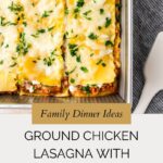 A pan of baked Ground Chicken Lasagna with zucchini, topped with melted cheese and chopped herbs. Next to the pan are a striped cloth and a white serving spatula on a light surface. Text overlay highlights this delicious recipe.