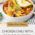 A bowl of ground chicken chili topped with shredded cheese, sliced avocado, and chopped cilantro, with a spoon on the side. Text overlay reads, Gluten Free Dinners: Chicken Chili with Ground Chicken.