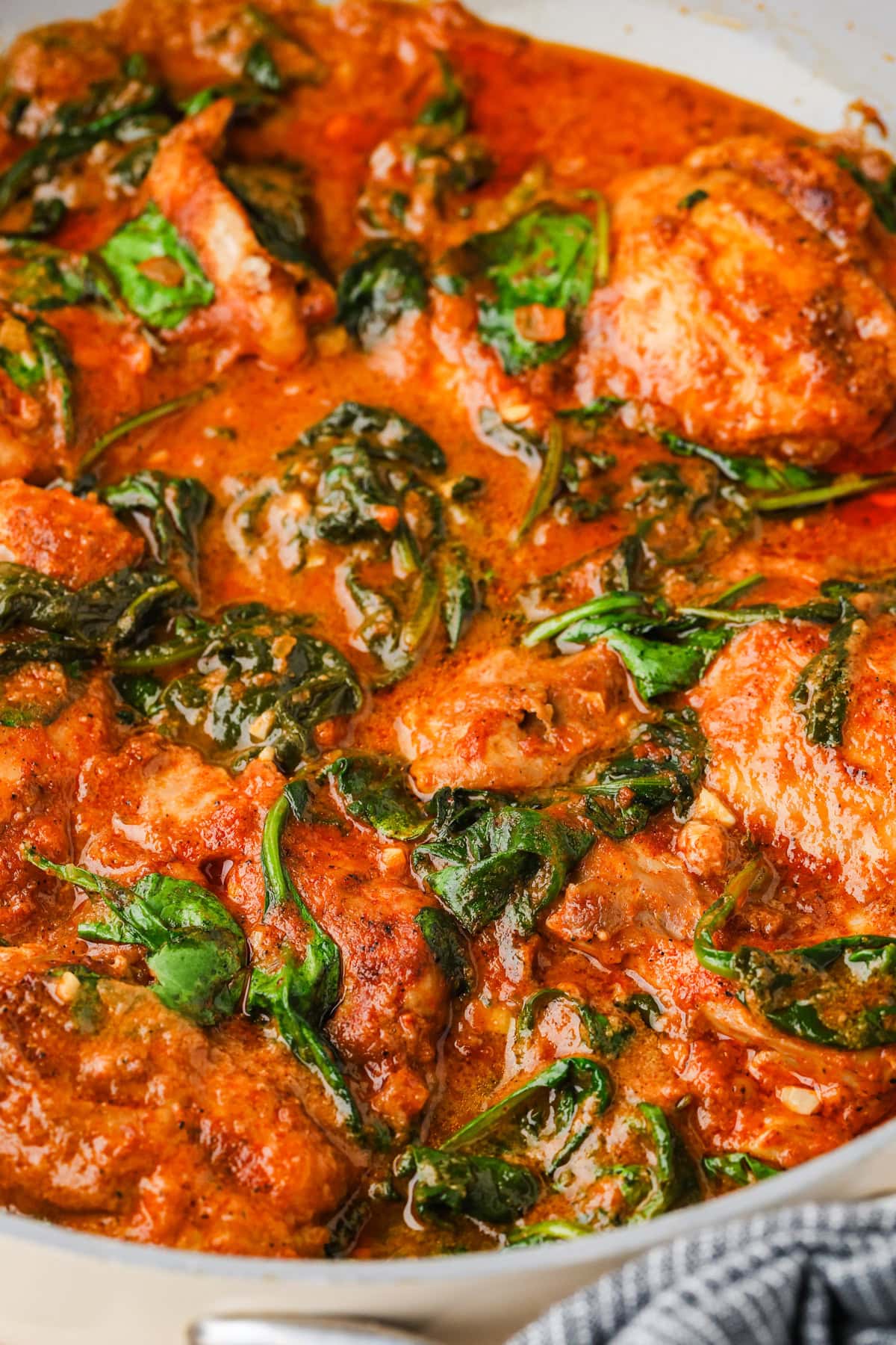 Chicken breasts cooked in a creamy tomato sauce with wilted spinach leaves, all in a pan. The dish is rich in color with visible seasoning and a thick, flavorful sauce.