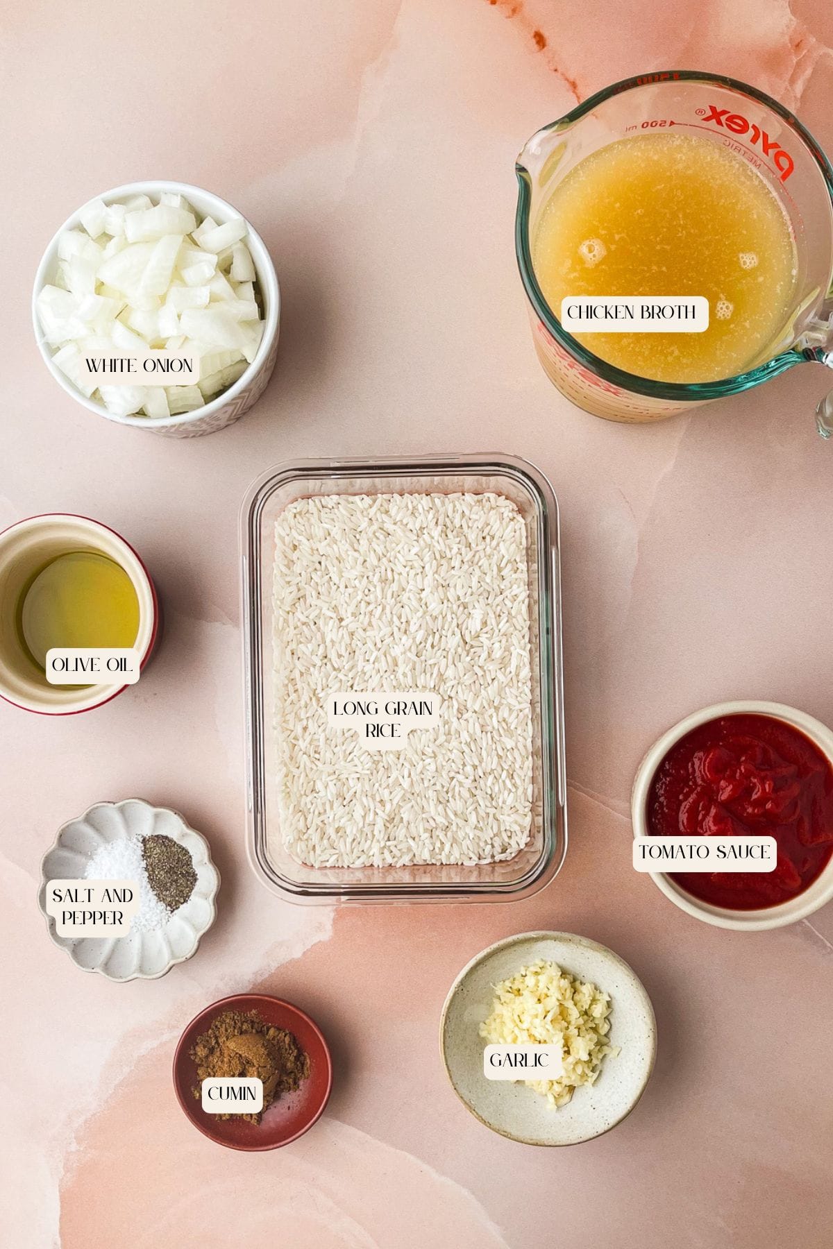 A flat lay of ingredients for spanish rice with tomato sauce: diced white onion, chicken broth in a measuring cup, tomato sauce, minced garlic, cumin, salt and pepper, olive oil, and a container of long grain rice on a pink surface.