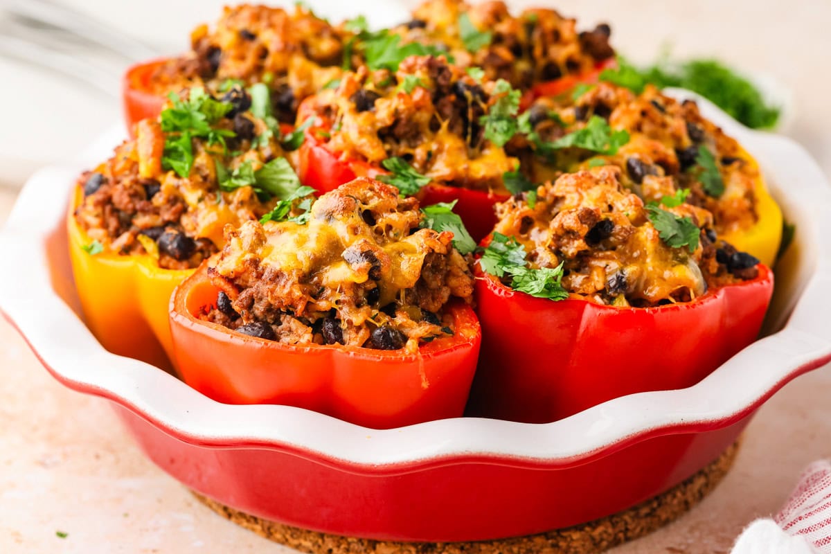 A round dish filled with red and yellow bell peppers stuffed with a mixture of ground meat, black beans, melted cheese, and topped with fresh chopped parsley.