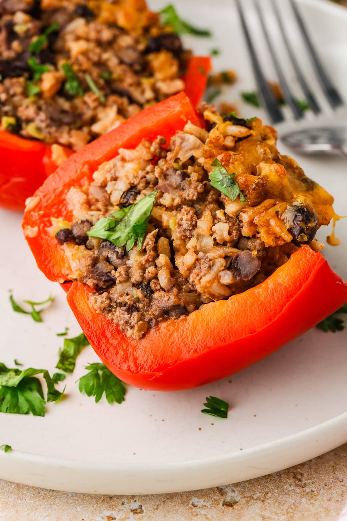 A close-up of a stuffed red bell pepper filled with a mixture of ground meat, rice, black beans, and topped with fresh chopped cilantro on a white plate with a fork in the background.