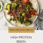 A bowl of white rice topped with bison stir fry, featuring broccoli, red bell peppers, green onions, and sesame seeds. Text reads: High Protein Bison Stir Fry at whensaltyandsweetunite.com.